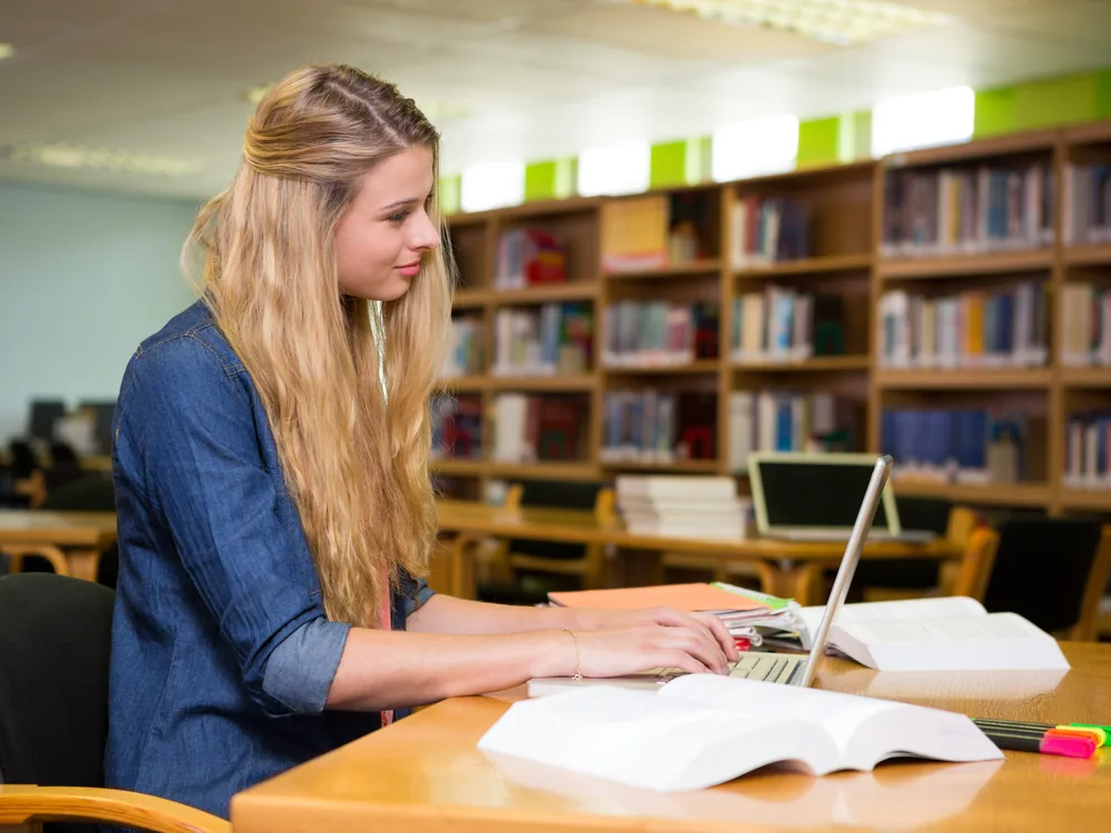 Student studying with books and a laptop in a library